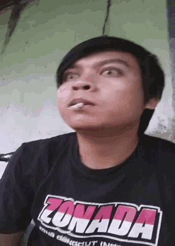 a man wearing a black shirt that says zonada smoking a cigarette