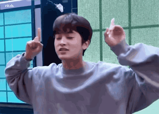 a young man in a grey sweater is making a middle finger gesture