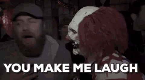 a clown is talking to a man in a dark room while holding a glass of beer .