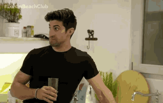 a man in a black shirt is holding a glass of water in his hand .