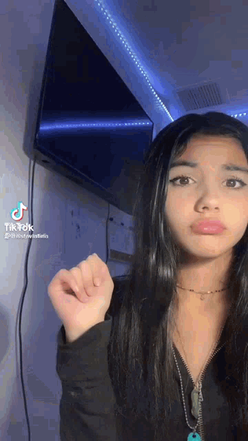 a girl with long black hair is standing in front of a television and making a funny face .