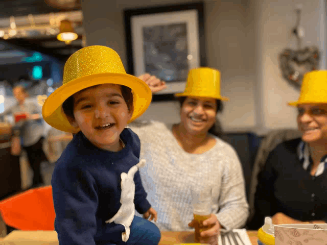 a little boy wearing a yellow hat sits at a table with two women