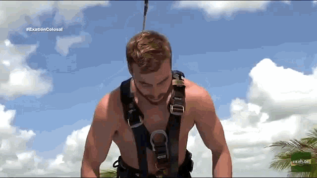 a man without a shirt is wearing a harness while standing in front of a blue sky .