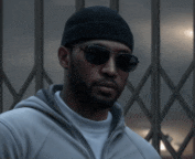 a man wearing sunglasses and a beanie is standing in front of a fence