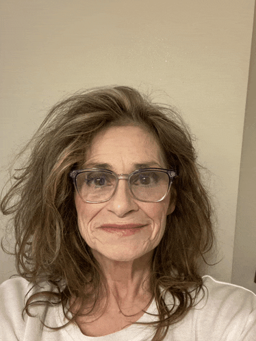 a woman wearing glasses and a white shirt looks at the camera