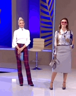 two women are standing next to each other on a stage . one of the women is holding a purse .