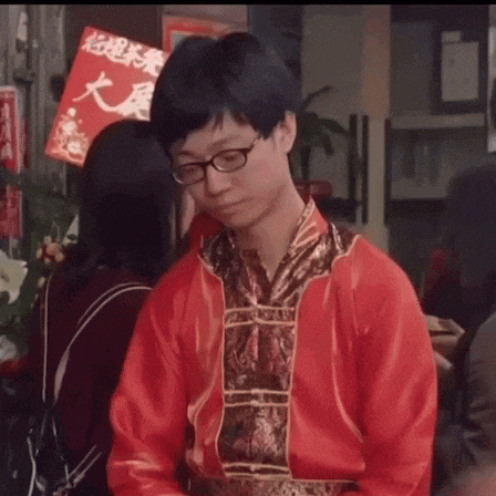 a man wearing glasses and a red jacket is talking to a woman in a crowd .