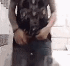 a man in a tank top is standing in a room holding his pants up .