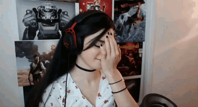 a woman wearing headphones is covering her face in front of a wall with posters of video games