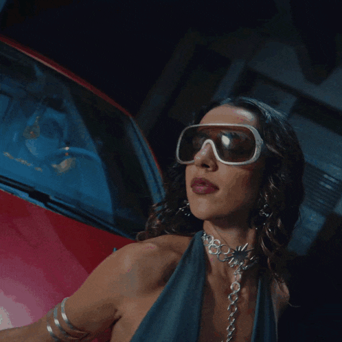 a woman wearing sunglasses and a choker is standing next to a red car