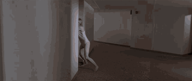 a woman in a bathing suit is running through a hallway with a red exit sign above her head