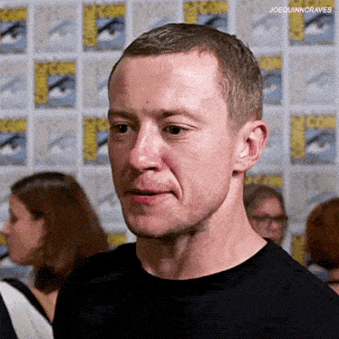 a man in a black shirt is making a funny face in front of a comic con wall .