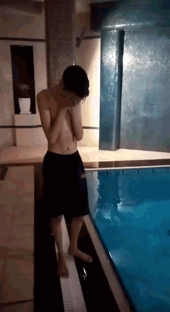 a shirtless man standing next to a swimming pool .