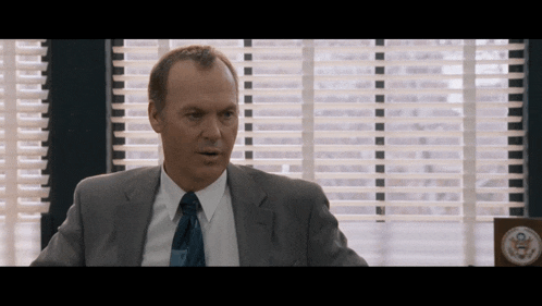 a man in a suit and tie sitting in front of a window