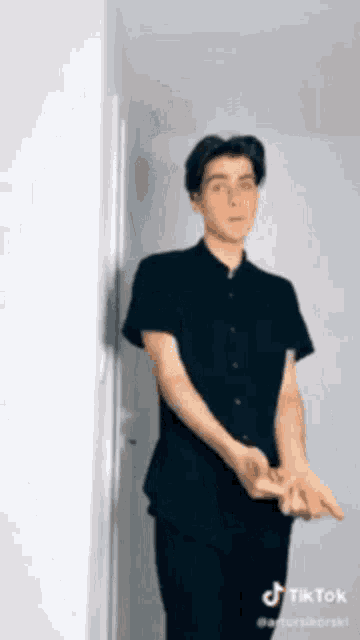 a young man in a black shirt and black pants is standing next to a wall .
