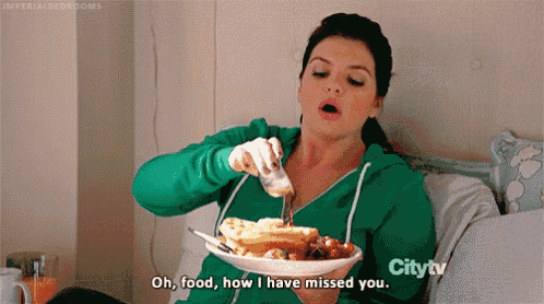 a woman is sitting on a bed eating waffles and strawberries while pouring syrup on them .