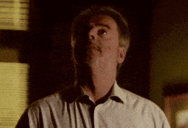 a man with a beard and a white shirt is looking up at something in the dark .