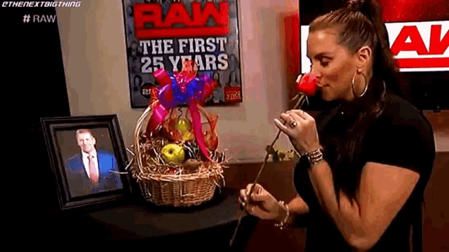 a woman is smelling a rose in front of a picture of a man and a sign that says raw the first 25 years