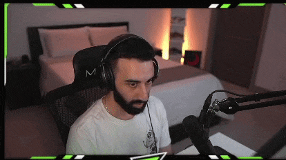 a man with a beard is wearing headphones while sitting in front of a microphone in a bedroom .