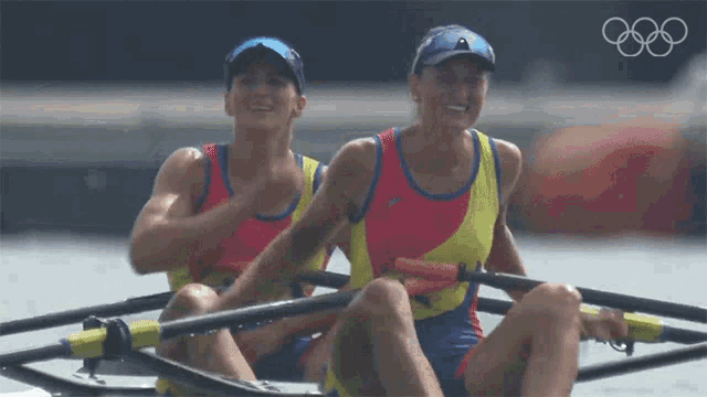 two people in a rowing boat with the olympic rings in the background