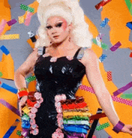 a drag queen is wearing a black dress with a rainbow of ribbons around her waist