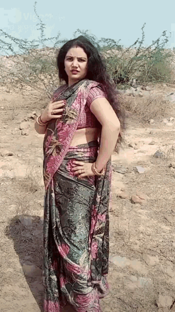 a woman in a saree is standing in the dirt in the desert .