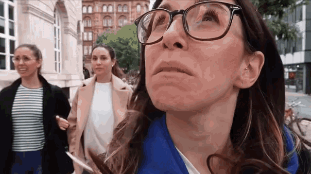 a woman wearing glasses and a blue jacket looks up at something