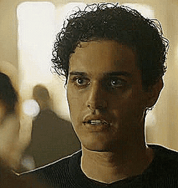 a man with curly hair is wearing a black shirt and looking at the camera with a serious look on his face .
