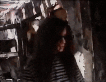 a woman with long hair and sunglasses is standing in a room .