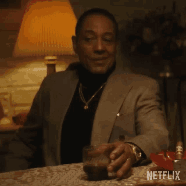a man in a suit is sitting at a table with a glass of whiskey in his hand .