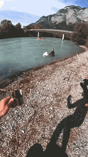 a person is holding a cup in front of a body of water with mountains in the background