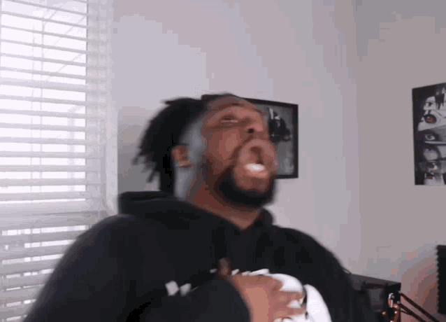 a man with a beard is making a funny face in front of a window in a room .
