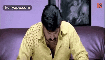 a man in a yellow shirt is sitting on a couch and looking down .