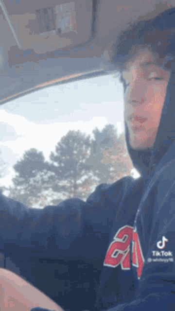 a young man wearing a hoodie is driving a car with his eyes closed .