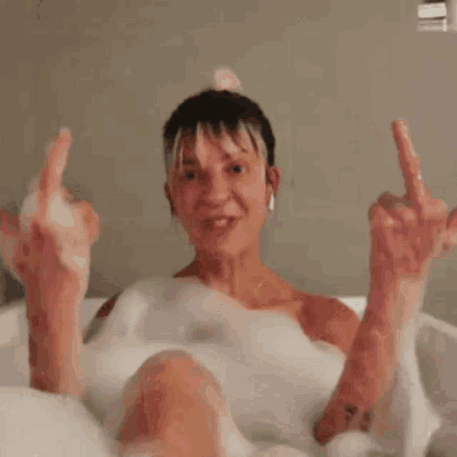 a woman in a bathtub with a tattoo on her arm is giving the middle finger