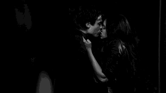 a black and white photo of a man and a woman kissing in a dark room .