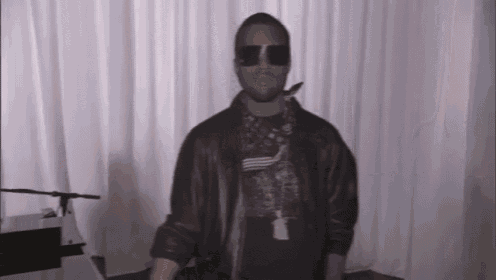 a man wearing sunglasses and a leather jacket is standing in front of a piano .