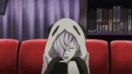 a girl is sitting on a red couch wearing a panda hoodie .