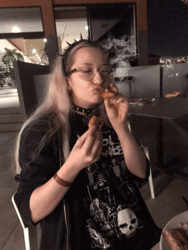 a girl wearing a black shirt with a skull on it is eating a pizza