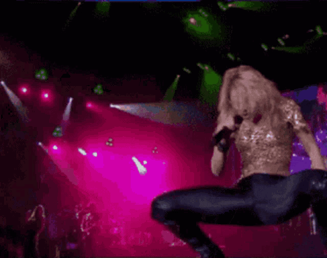 a woman singing into a microphone on a stage with pink lights