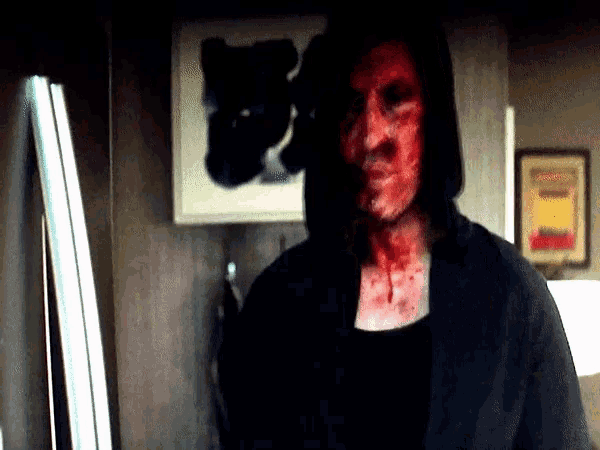 a man with blood on his face stands in front of a framed picture