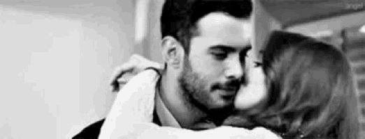 a black and white photo of a man and a woman kissing .