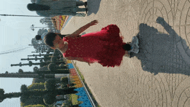a little girl in a red dress is walking down a brick sidewalk