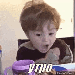 a little boy is sitting at a table with a purple cup and the word ytpo on his face