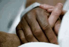 a close up of two people holding hands in a hospital bed .