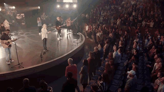 a group of people are singing and playing guitars in front of a crowd