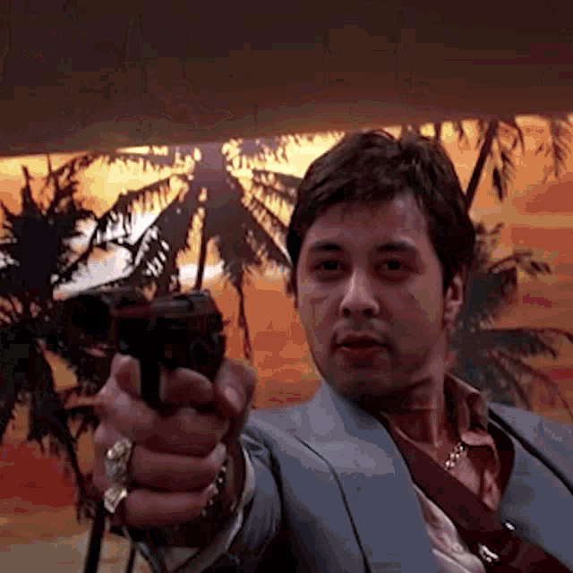 a man in a suit holds a gun in front of a palm tree painting