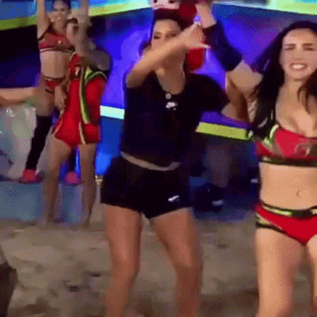 a group of women in bikinis are dancing on a stage in front of a crowd .