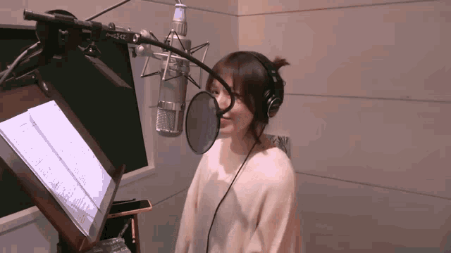 a woman wearing headphones is singing into a microphone in a room with a book on a stand