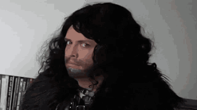 a man with long hair and a beard is wearing a wig and making a funny face .